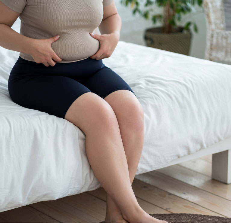 mishawaka woman sitting on bed pinching tummy before a tummy tuck